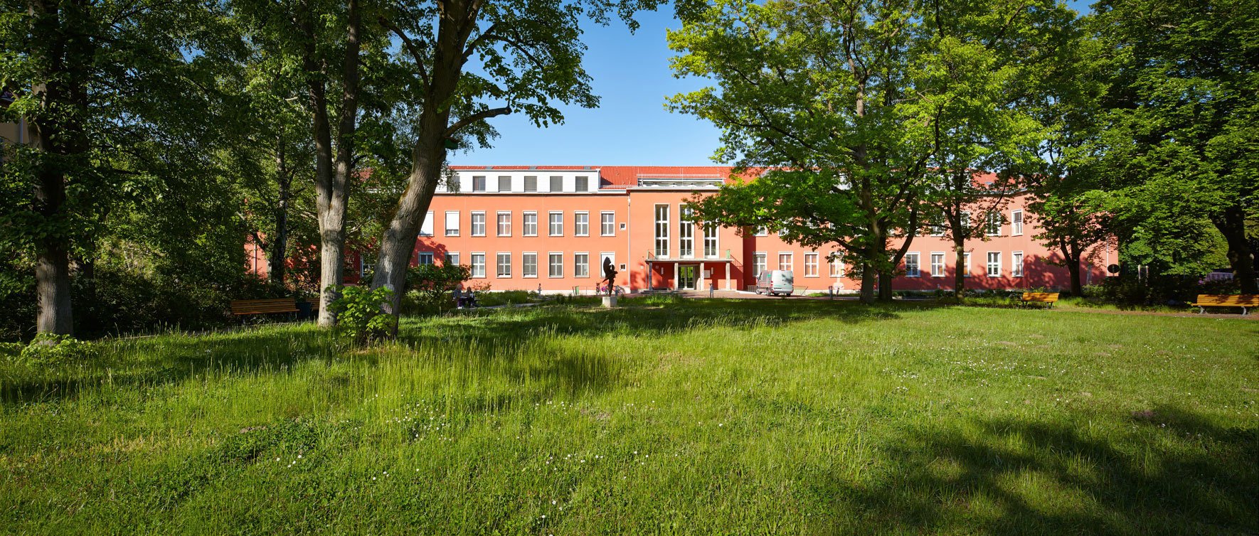 Rotes Hauptgebäude des Gemeinschaftskrankenhauses Havelhöhe umgeben von üppigen Grünflächen
